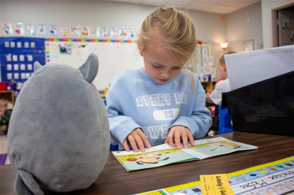 student reading to gray stuffed animal